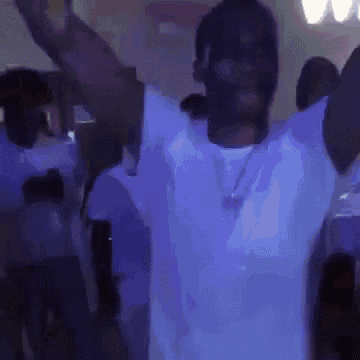 a man in a white shirt is dancing in a dark room with his arms in the air .
