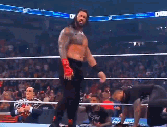 roman reigns is standing in the middle of a wrestling ring with his arms outstretched
