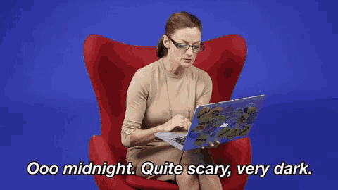 a woman is sitting in a red chair using a laptop and says " ooo midnight quite scary very dark "