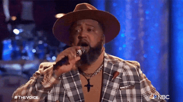 a man with a beard is singing into a microphone while wearing a plaid jacket and a hat .