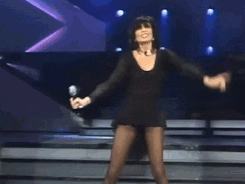 a woman in a black dress is singing into a microphone while dancing on a stage .