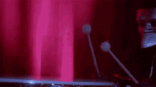 a person in a mask is playing drums in front of a red curtain .