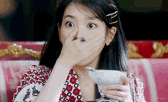 a woman is covering her mouth while holding a glass of wine .