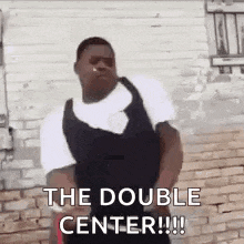 a man is standing in front of a brick wall smoking a cigarette and saying `` the double center '' .