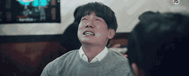 a man in a grey sweater is crying while sitting at a table .