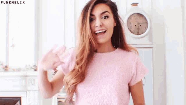 a woman in a pink shirt is waving at the camera .