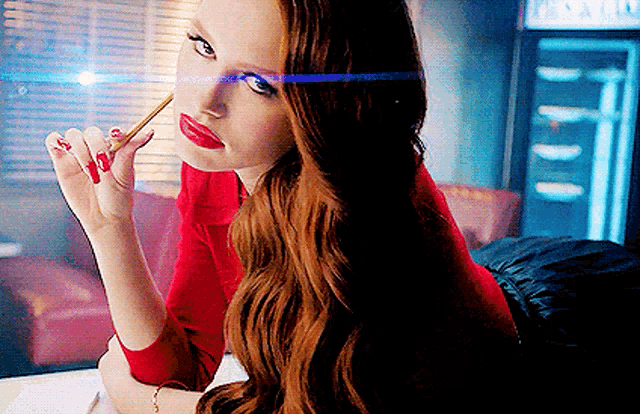 a woman in a red shirt is holding a pen in her mouth
