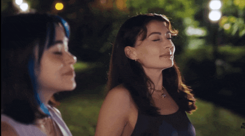 a woman with blue hair is standing next to another woman in a park at night
