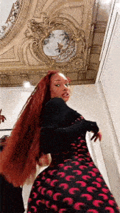 a woman with long red hair is standing in a room with a ceiling .