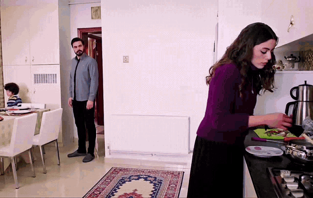 a woman in a purple sweater stands in a kitchen preparing food