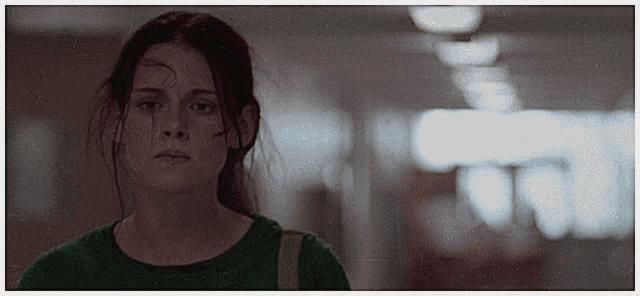 a woman in a green shirt stands in a dark hallway