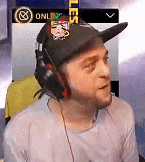 a man wearing headphones and a baseball cap is sitting in front of a computer screen .