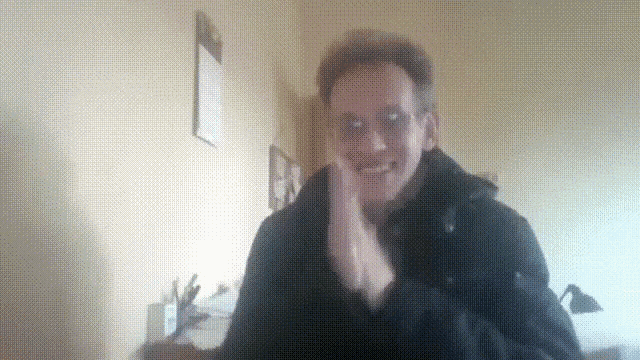 a man wearing glasses and a black jacket is smiling and clapping his hands