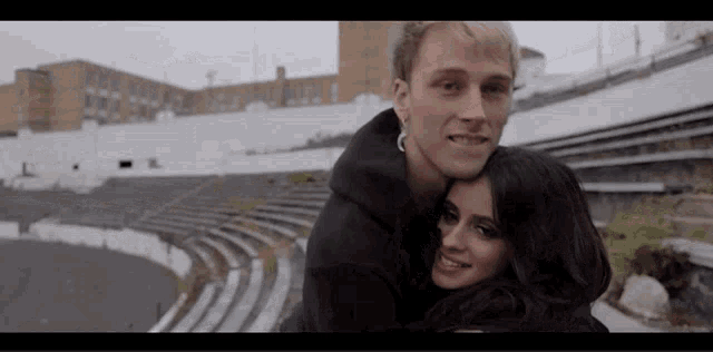a man and a woman are posing for a picture in front of a stadium .