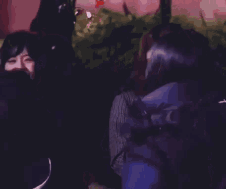 two women are standing next to each other in a dark room . one of the women is holding a glass of water .