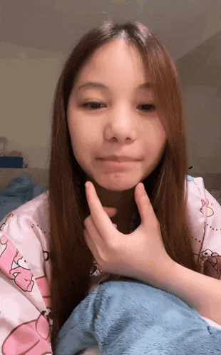 a young girl with long hair is sitting on a bed and touching her face .