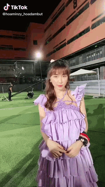 a woman in a purple dress is standing in front of a large orange building .