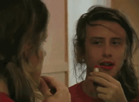 a woman is applying red lipstick to her lips while looking at herself in the mirror .