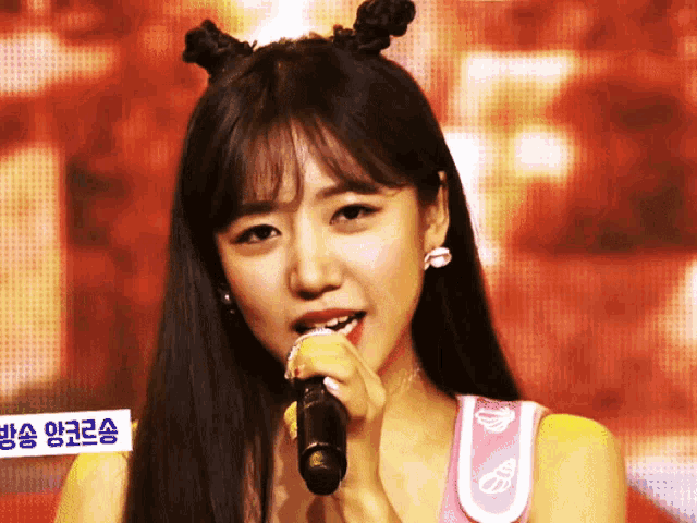 a woman singing into a microphone with a sign behind her that says ' korean '