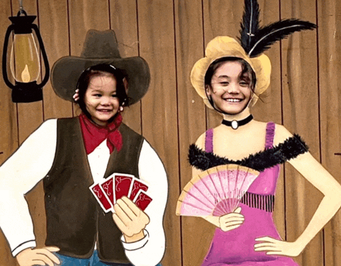 a little girl dressed as a cowboy and a little girl dressed as a lady with a fan