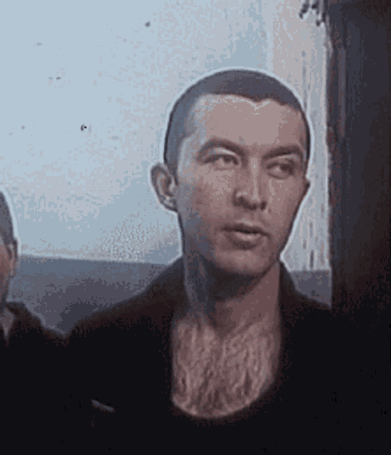 a man with a shaved head is standing in front of a window looking at the camera .