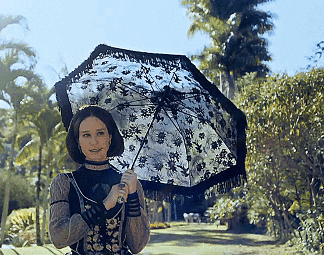 a woman in a black dress holds a black and white floral umbrella