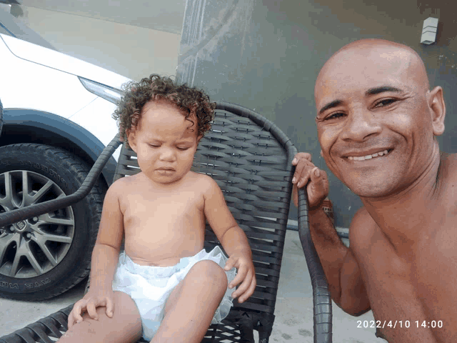 a man holds a baby in a diaper in front of a car on a date of 2022/4/10