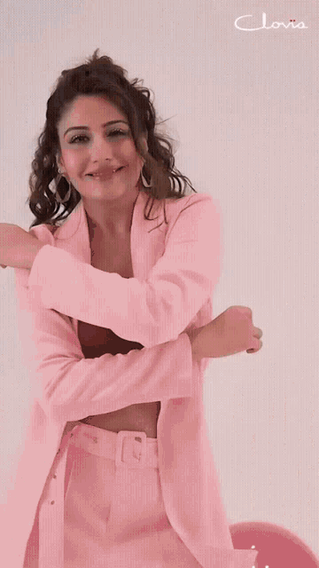 a woman in a pink suit is standing in front of a white wall with the word clovia on it