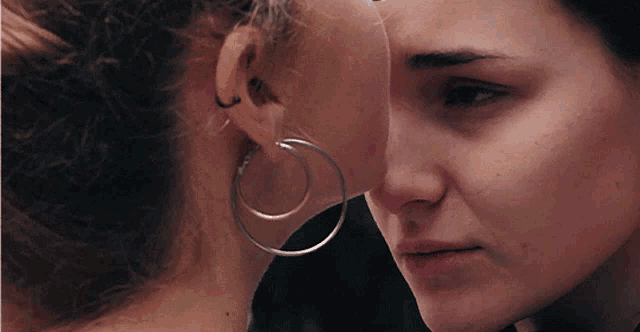 a woman wearing hoop earrings is whispering something into another woman 's ear