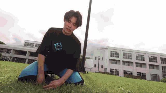 a man wearing a black shirt with the word slim on it is kneeling on the grass