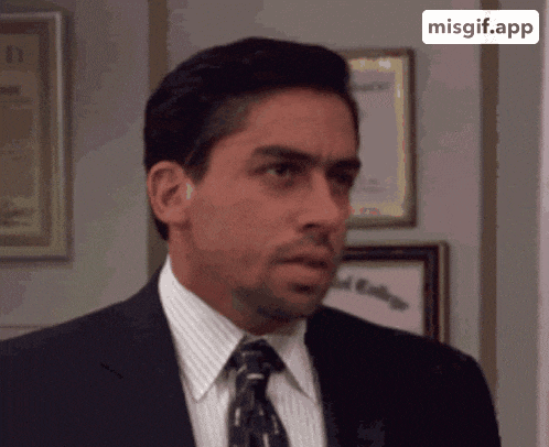 a man in a suit and tie is looking at the camera with a misgif.app icon behind him