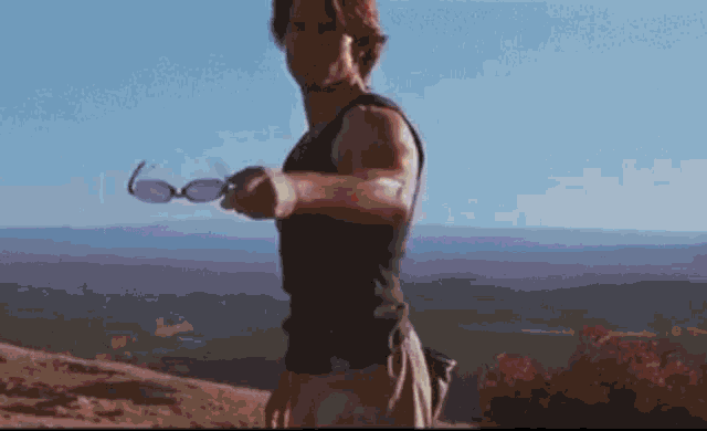 a man is standing on top of a hill holding a pair of sunglasses .