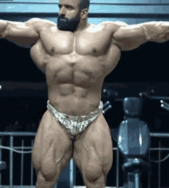 a man with a beard is standing in a gym with his arms outstretched .