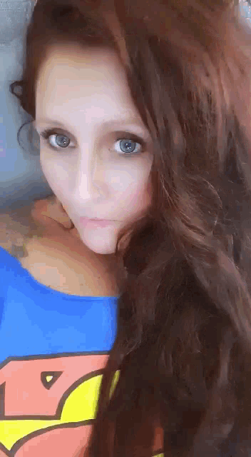 a woman with long hair is wearing a blue shirt with a superman logo on it