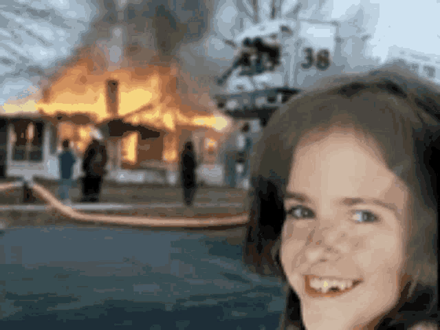 a girl is smiling in front of a burning house .