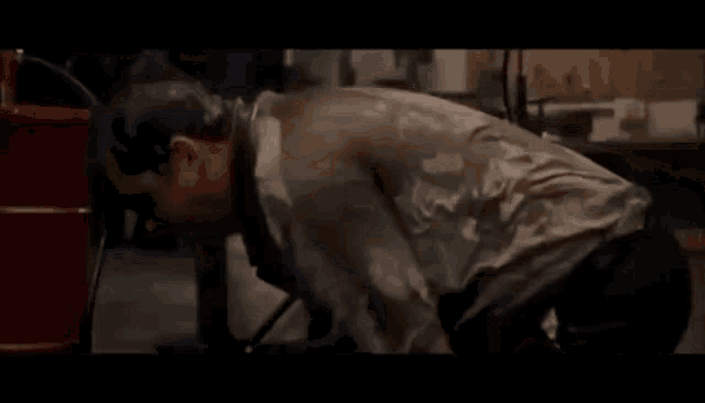 a man is kneeling down in front of a red barrel in a garage .