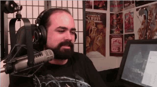 a man with a beard is wearing headphones in front of a microphone with a queen poster in the background