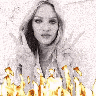 a woman is making a peace sign with her hands in front of fire .