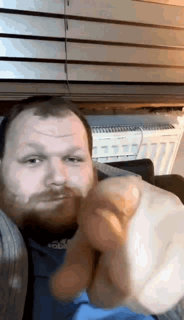 a man with a beard wearing a shirt that says adidas is pointing at the camera