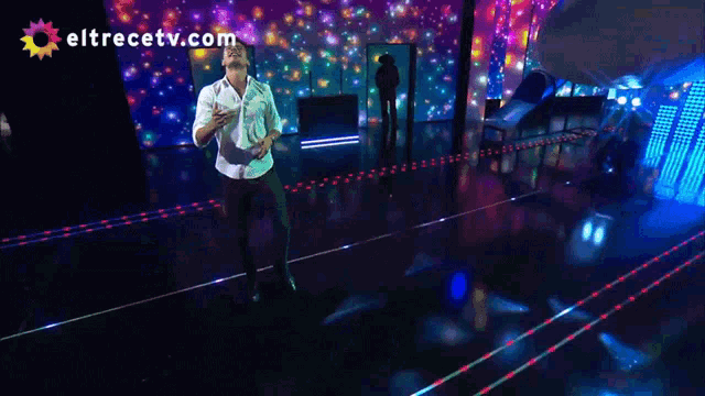 a man in a white shirt is dancing on a stage with eltrecetv.com in the background