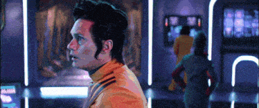 a man in an orange jacket stands in a room
