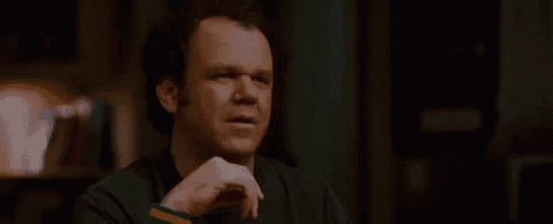 a man is sitting at a table talking to another man while holding a cell phone .