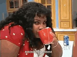 a woman is drinking from a red cup while sitting at a table in a kitchen .