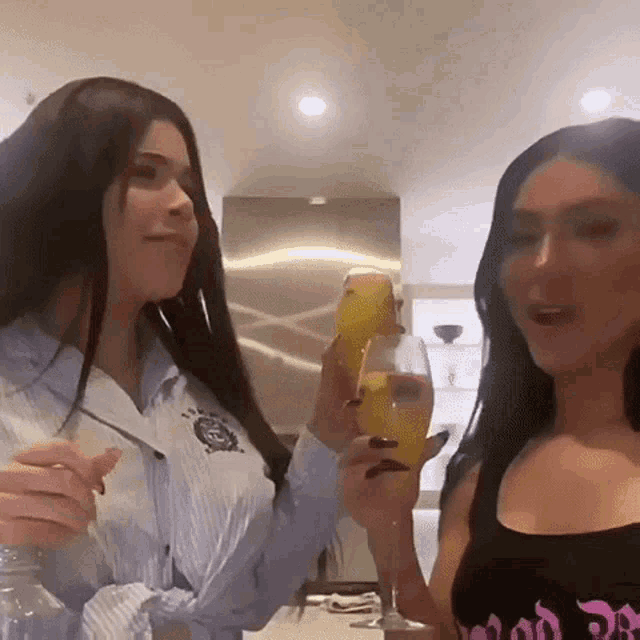 two women are standing next to each other in a kitchen holding glasses of orange juice .