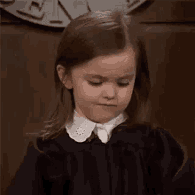 a little girl wearing a black dress and white tie is making a funny face .