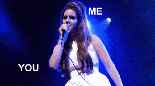 a woman in a white dress is singing into a microphone on a stage with the words `` me you '' behind her .
