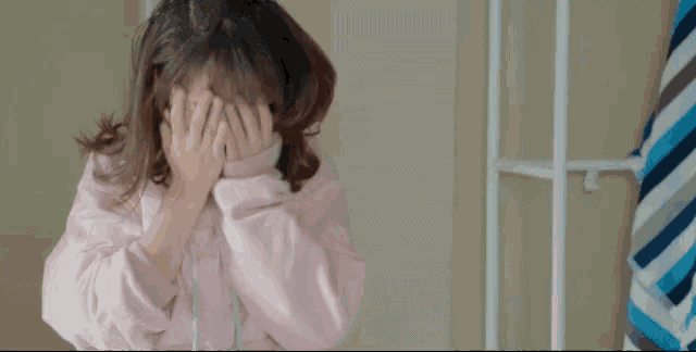 a woman covering her face with her hands in front of a striped towel