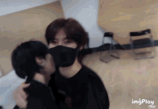 a man wearing a black mask kisses another man
