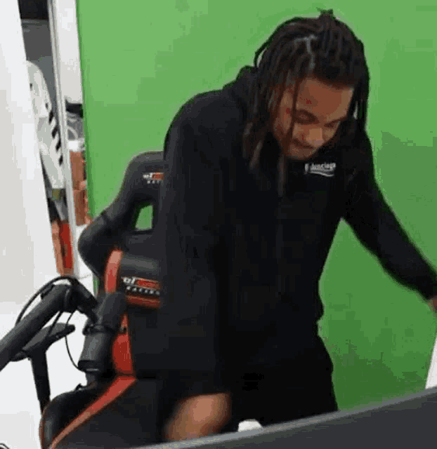 a man with dreadlocks is sitting in a chair in front of a green background .