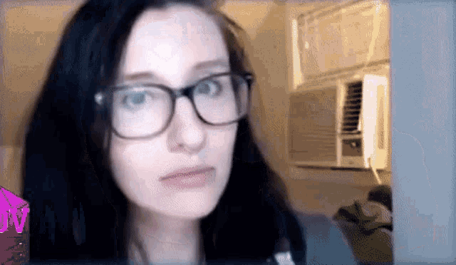 a woman wearing glasses is standing in front of an air conditioner and a purple jv logo